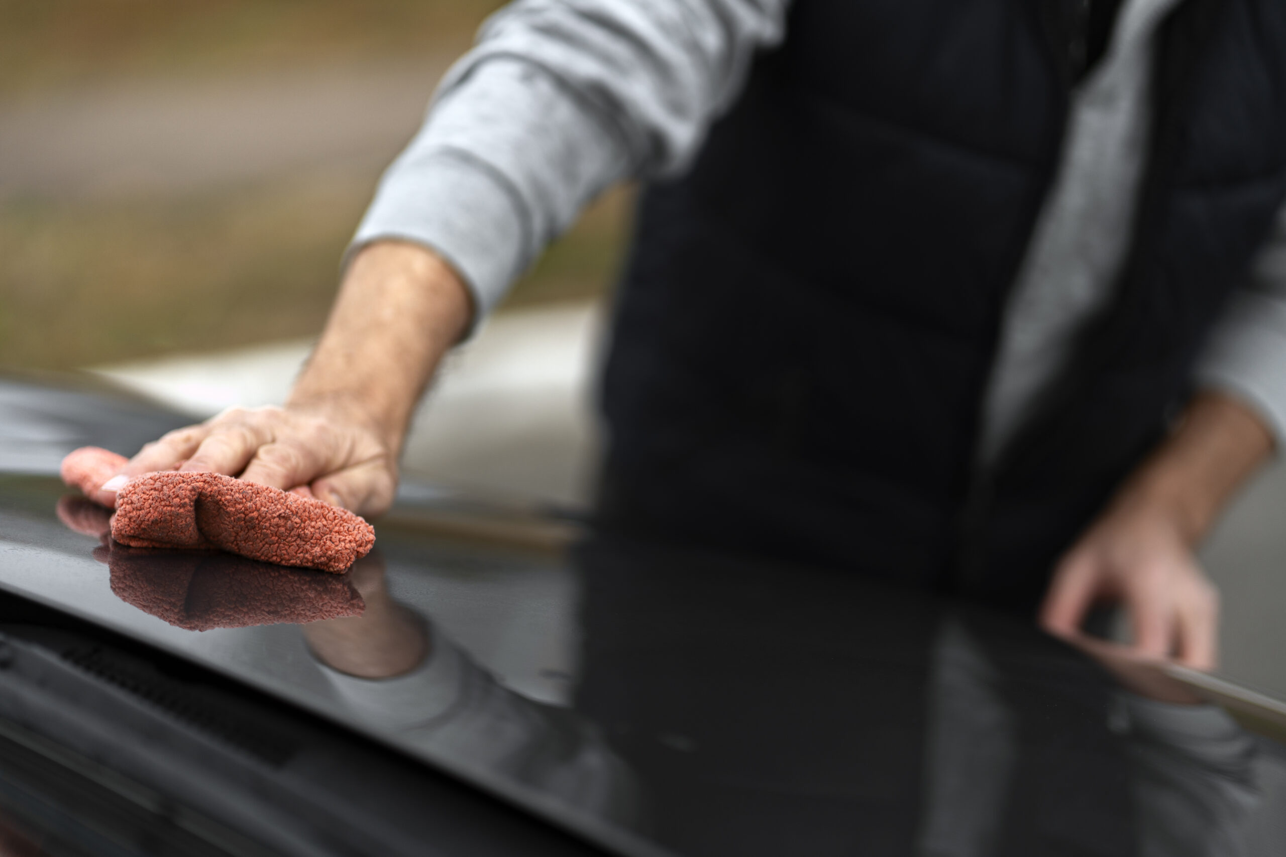 Car detailing - man holding the microfiber cloth in hand and polishing the car. Selective focus.